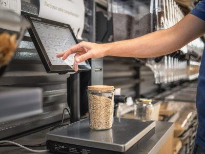 Balance libre-service VRAC un homme pèse un récipient de riz sur une balance tactile dans une épicerie bio